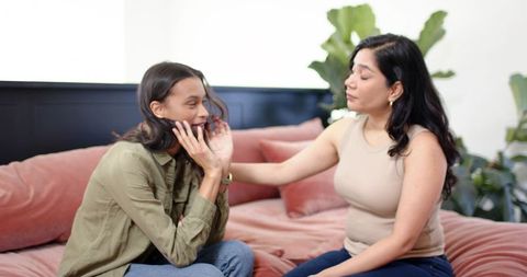 Diverse women comforting each other on plush pink bed, sharing support and empathy