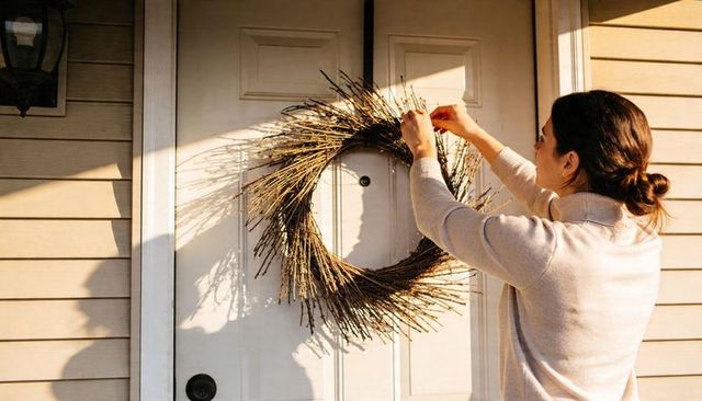 Hanging and adjusting rustic twig wreath on white paneled front door in warm sunlight