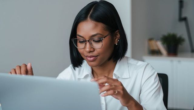 Focused black businesswoman wearing glasses typing on laptop in minimalist office