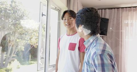 Man and teen standing by open casement window in sunlit living room with garden view