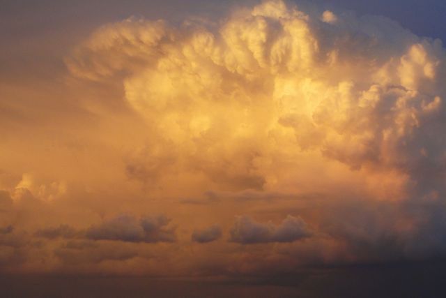 Golden cumulonimbus clouds illuminated by sunset, creating a dramatic and captivating sky scene. Perfect for use in weather-related graphics, nature documentaries, environmental presentations, or relaxing background imagery.