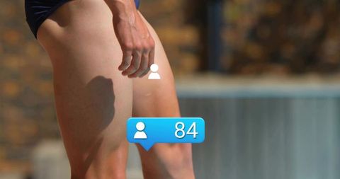 Male swimmer standing poolside in dark briefs showing muscular thighs with social badge