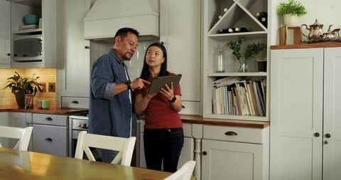 Asian couple using tablet to plan kitchen remodel in cozy modern home