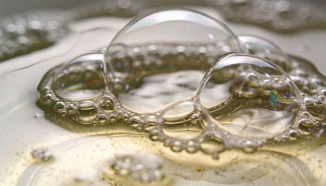 Macro golden liquid showing linked clear bubble cluster with soft iridescent reflections