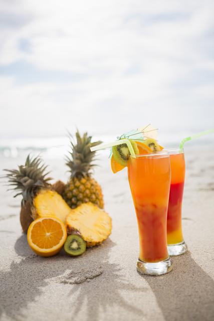 Two glasses of cocktail drink and tropical fruits kept on sand at tropical beach