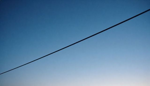 Single utility cable cutting diagonal across clear blue gradient sky at sunrise