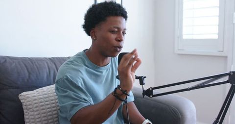 Young host hosting casual home podcast while speaking, gesturing and recording with microphone