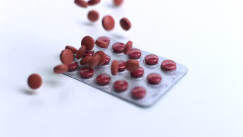 Red Tablets Falling on Blister Pack in Slow Motion