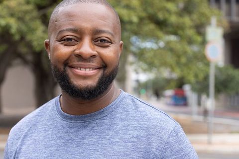 Smiling african man standing on city sidewalk wearing casual gray t-shirt and silver chain