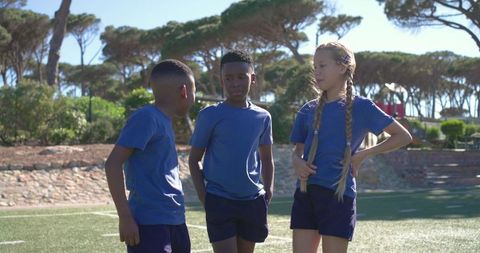 Young teammates standing and talking on sunlit turf field wearing blue uniforms