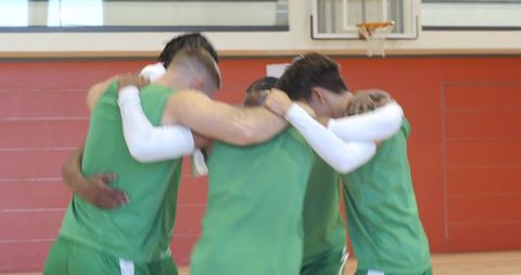Diverse basketball teammates huddling under hoop showing unity, camaraderie, motivation