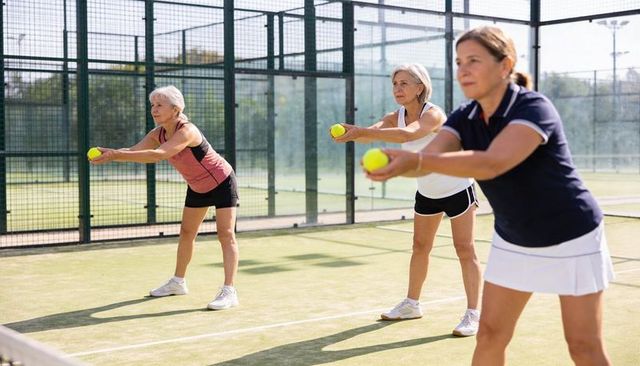 Senior women practicing padel technique holding tennis balls on outdoor court