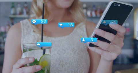 Blonde woman checking phone sipping mint-lime cocktail at bar with social media notifications