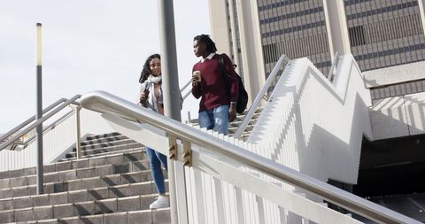 Diverse friends walking down urban zigzag staircase with coffee and smartphone commuting