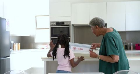 African american grandmother and granddaughter sorting glass recycling in modern kitchen