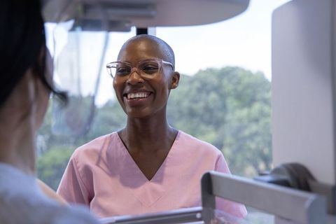 Smiling african american nurse talking through protective partition in pink scrubs