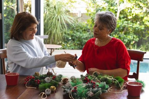 Joyful senior women crafting wreaths together by sunlit window