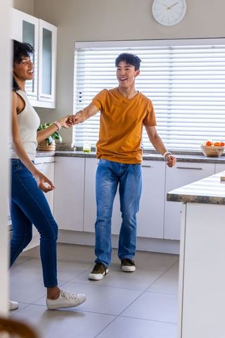 Diverse couple holding hands while asian man checking wristwatch in modern kitchen