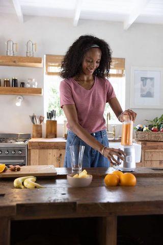 Smiling african american woman blending orange smoothie on rustic kitchen island