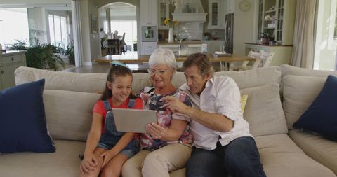 Happy Grandparents with Granddaughter Using Tablet at Home