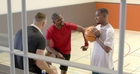 Multiracial basketball teammates chatting and strategizing while resting on gym bleachers