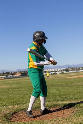 Baseball player swinging bat in green yellow uniform at sunny ballpark
