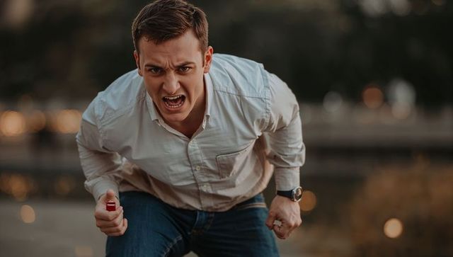 Shouting man leaning forward holding red spray canister confronting on waterfront at dusk