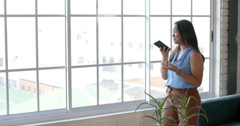 Middle-Aged Businesswoman Communicating on Smartphone by Window