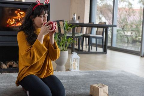 Woman enjoys hot beverage by fireplace wearing festive antler headband