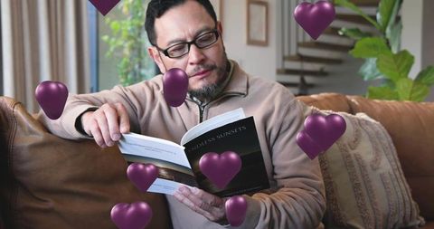 Mature asian man reading endless sunsets on leather sofa with purple heart overlays