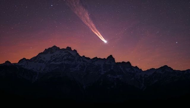 Comet streaking over snowy alpine peaks at twilight, starfield trail across indigo sky