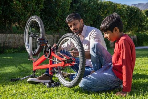 Father Helping Son Repair Bicycle on Outdoor Lawn