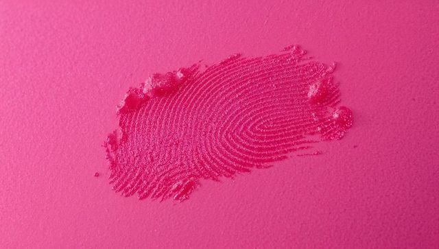 Magenta fingerprint impression revealing ridge detail on pink matte surface macro texture