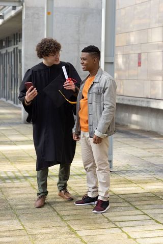 Graduating student celebrating with friend on campus walkway smiling and chatting