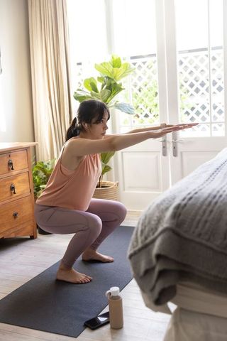 Woman practicing squat pose on mat in bright bedroom home workout morning routine
