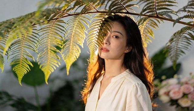 Young woman standing beneath fern fronds backlit by warm golden light