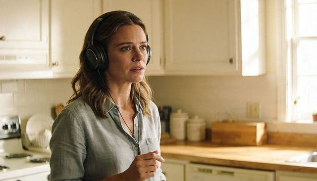 Woman listening with over-ear wired headphones in sunlit modern kitchen