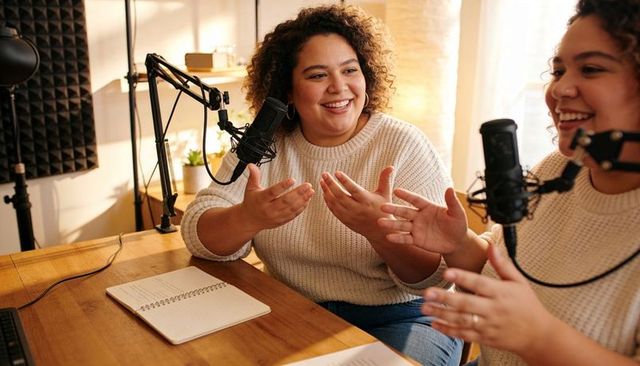 Smiling cohosts recording conversational podcast in cozy home studio with condenser mics