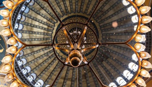 Ornate metal chandelier radiating warm bulbs under vaulted dome with clerestory windows