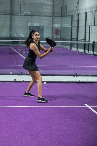 Indian woman playing padel on vibrant purple indoor court holding paddle in ready stance