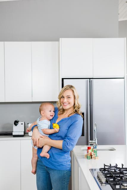 Smiling Mother Holding Baby in Modern Home Kitchen - Download Free Stock Photos Pikwizard.com