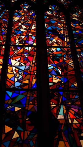 Vertical video showing sunlight shifting through gothic stained glass mosaic with lead lines