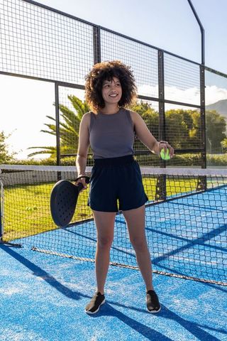 Woman playing padel on vibrant blue court holding racket and ball in sunny outdoors