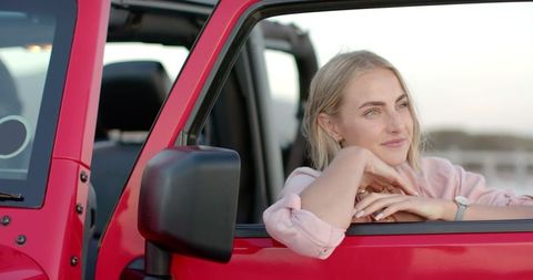 Relaxed woman enjoying road trip in red convertible at sunset