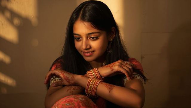 Young indian woman wearing embroidered kurta and bangles, showcasing henna in golden light