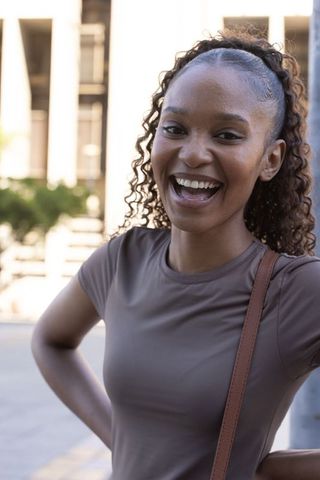 Laughing african woman wearing taupe t-shirt and shoulder bag urban street portrait