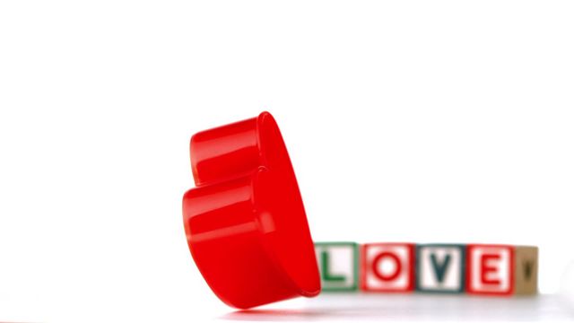 This image features a red heart ornament spinning in slow motion, positioned in front of blocks spelling out 'LOVE.' Perfect for use in romantic-themed advertisements, newsletters or website design focusing on romance, relationships, and gift messages. Ideal for Valentine's Day promotions or articles exploring the theme of love.