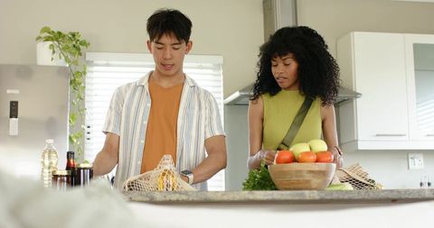Multiethnic couple unpacking groceries and arranging fresh produce on modern kitchen island