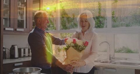 Senior Man Surprising Woman with Roses in Kitchen