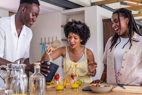 African american friends making fruit cocktails at kitchen island laughing and serving
